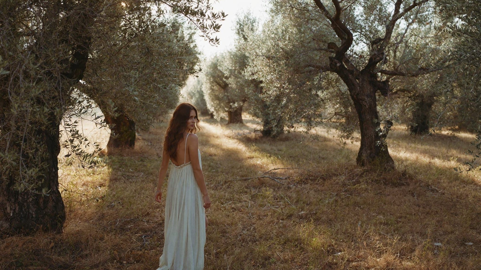 A woman in an ivory linen dress walking through an olive grove