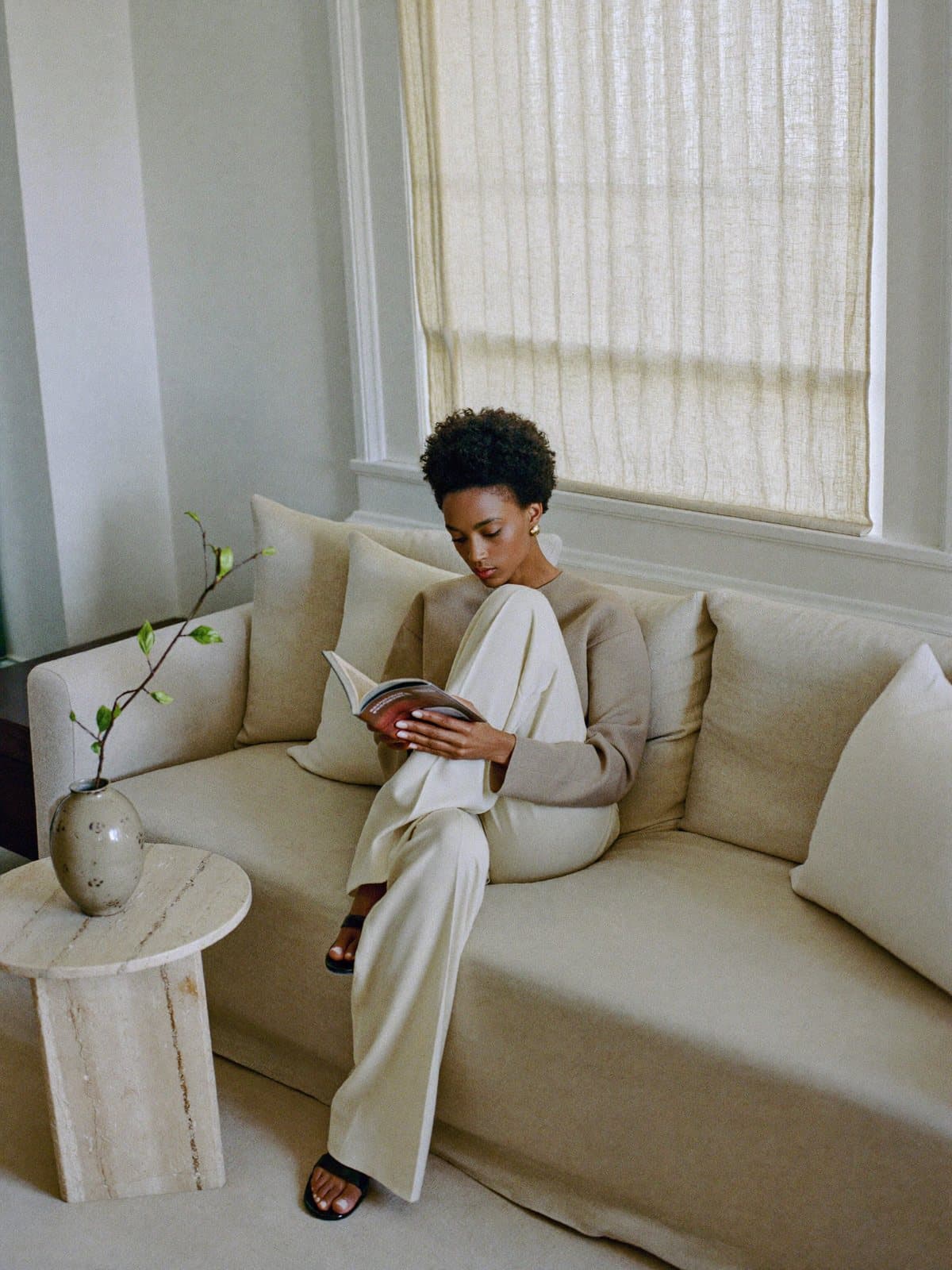 A woman reading on a linen sofa in soft window light